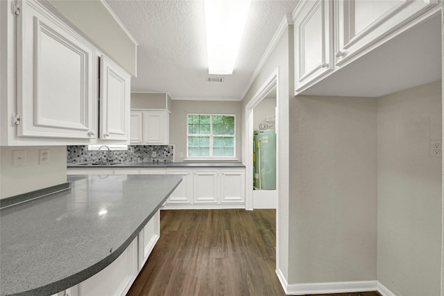 kitchen with ornamental molding, a textured ceiling, dark wood-type flooring, sink, and white cabinets