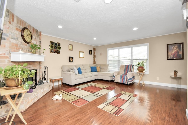 living room with ornamental molding, dark wood-type flooring, a textured ceiling, and a brick fireplace