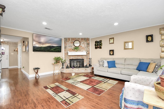 living room featuring dark hardwood / wood-style floors, crown molding, a textured ceiling, and a brick fireplace