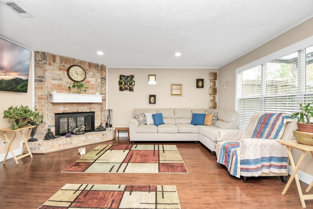 living room with a textured ceiling, a brick fireplace, and dark wood-type flooring