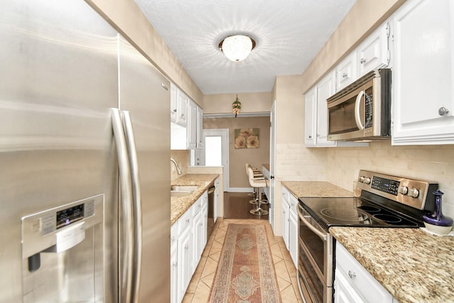 kitchen with decorative backsplash, light tile patterned flooring, white cabinetry, and appliances with stainless steel finishes