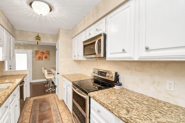 kitchen featuring light tile patterned flooring, light stone countertops, white cabinetry, and stainless steel appliances