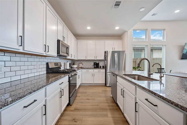 kitchen featuring white cabinets, sink, stainless steel appliances, and dark stone counters