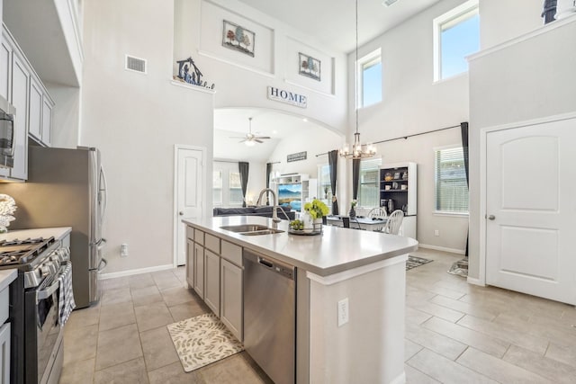 kitchen featuring ceiling fan with notable chandelier, stainless steel appliances, sink, decorative light fixtures, and an island with sink