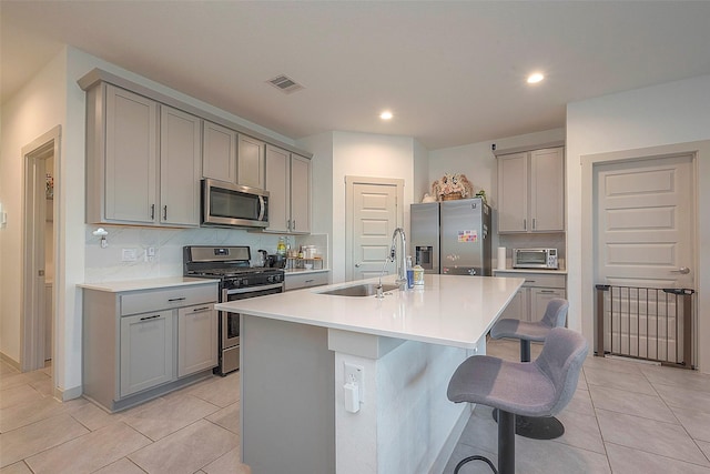 kitchen with visible vents, gray cabinets, a sink, appliances with stainless steel finishes, and a kitchen breakfast bar