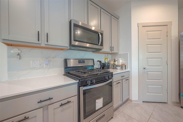 kitchen featuring stainless steel appliances, backsplash, gray cabinets, and light countertops