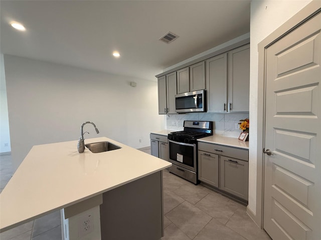 kitchen with tasteful backsplash, gray cabinets, appliances with stainless steel finishes, and a sink