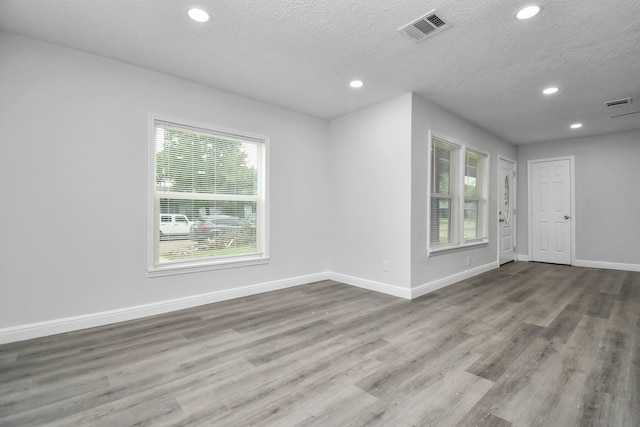 empty room featuring a textured ceiling, light wood-type flooring, and a healthy amount of sunlight