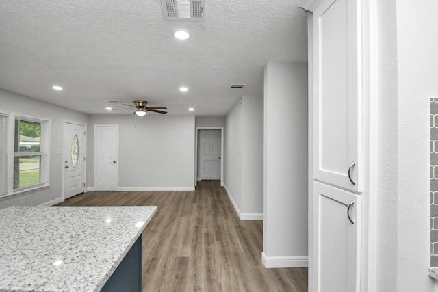 kitchen with a textured ceiling, light wood-type flooring, light stone counters, and ceiling fan