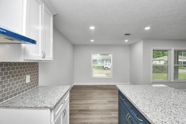 kitchen featuring a textured ceiling, light stone countertops, white cabinetry, and blue cabinetry