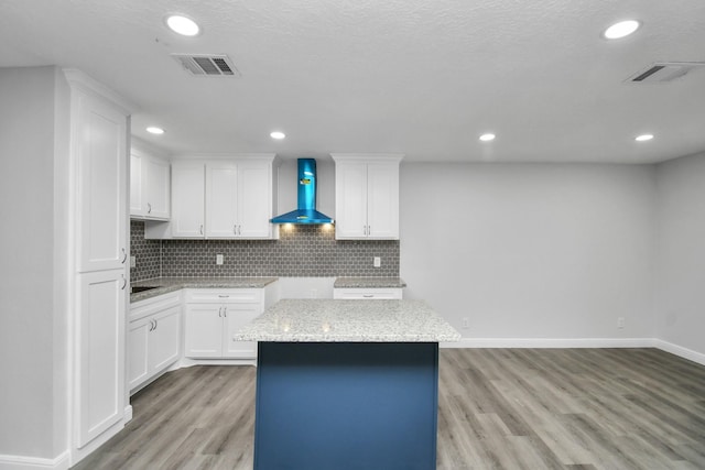 kitchen with white cabinetry, wall chimney exhaust hood, light wood-type flooring, and a kitchen island