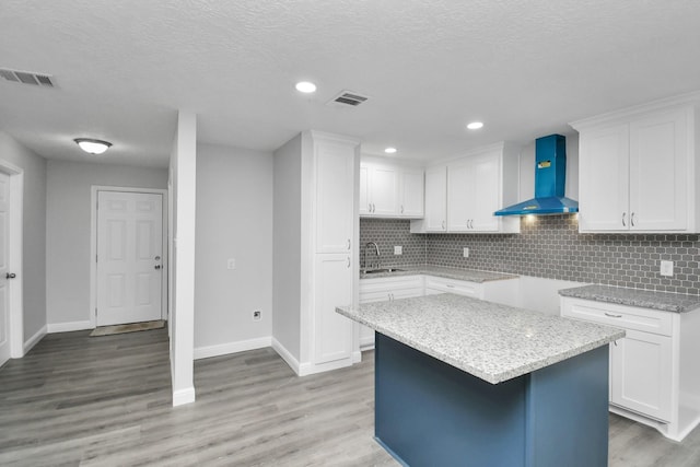 kitchen with backsplash, a center island, white cabinets, and wall chimney range hood