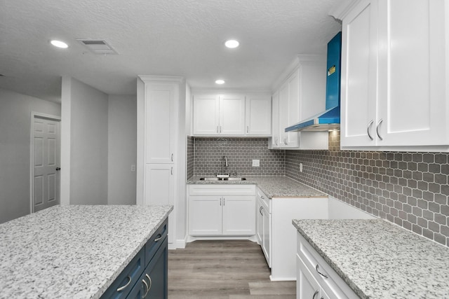 kitchen featuring backsplash, sink, white cabinets, and wall chimney range hood