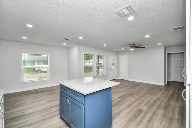 kitchen featuring light stone countertops, a textured ceiling, ceiling fan, hardwood / wood-style floors, and a center island