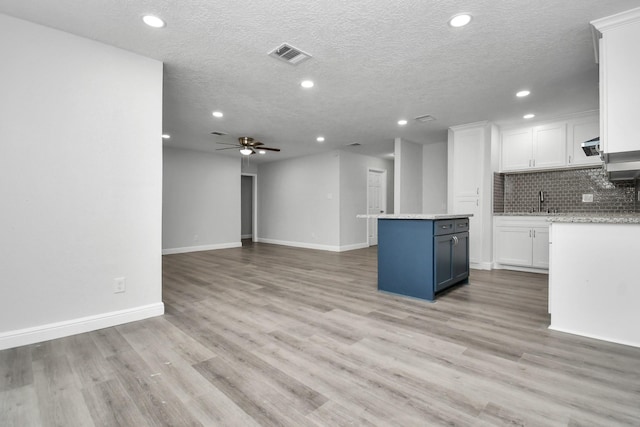 kitchen with decorative backsplash, ceiling fan, a center island, and white cabinets