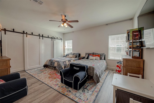 bedroom with a barn door, ceiling fan, and light wood-type flooring