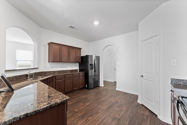 kitchen with dark wood-type flooring, sink, dark stone countertops, appliances with stainless steel finishes, and dark brown cabinetry