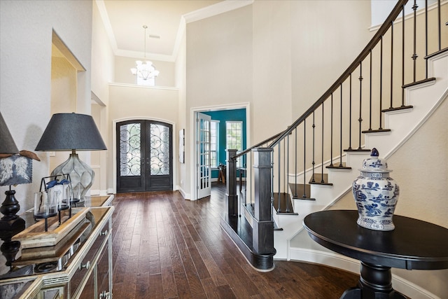 foyer with dark wood-type flooring, an inviting chandelier, french doors, crown molding, and a towering ceiling