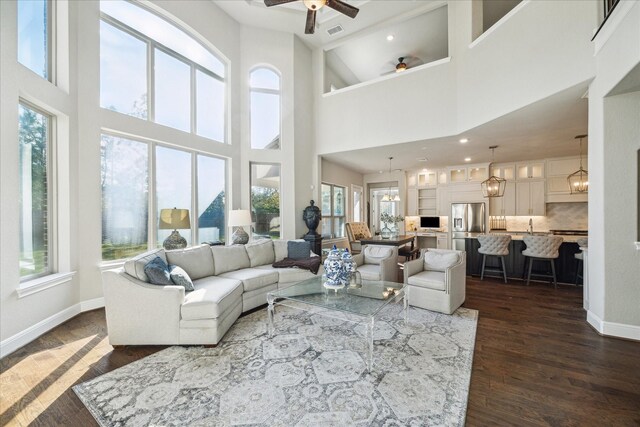 living room with a towering ceiling, dark wood-type flooring, and ceiling fan with notable chandelier