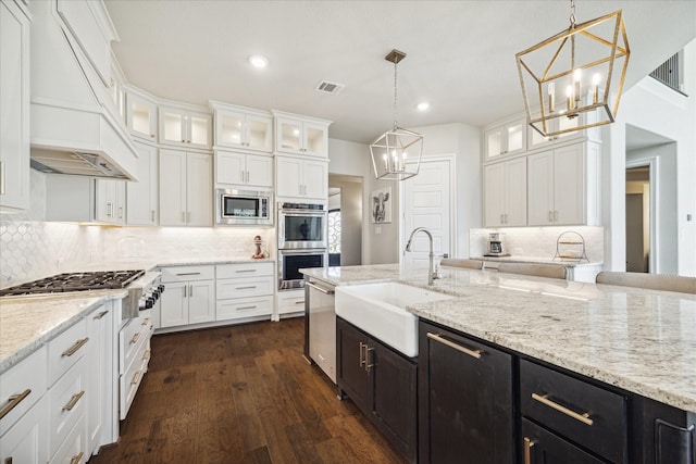 kitchen with sink, decorative light fixtures, white cabinets, custom range hood, and appliances with stainless steel finishes