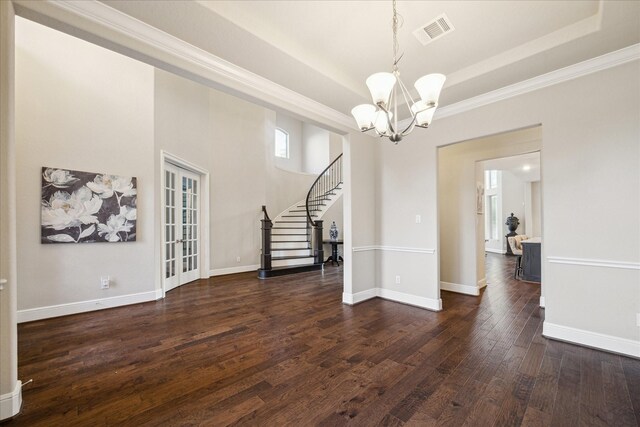 unfurnished dining area with a notable chandelier, a raised ceiling, ornamental molding, and dark wood-type flooring