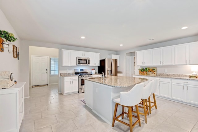 kitchen featuring light stone counters, a kitchen island with sink, a breakfast bar, white cabinets, and appliances with stainless steel finishes