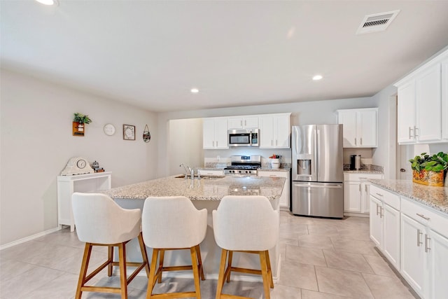 kitchen featuring an island with sink, appliances with stainless steel finishes, light stone counters, white cabinetry, and a breakfast bar area