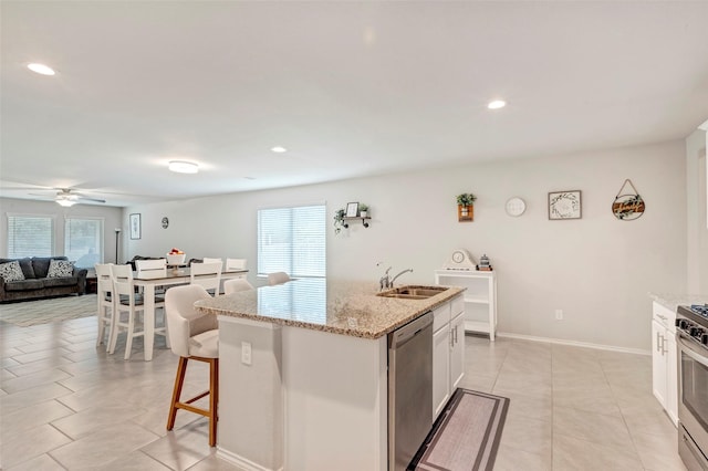 kitchen featuring a center island with sink, white cabinets, sink, light stone counters, and stainless steel appliances