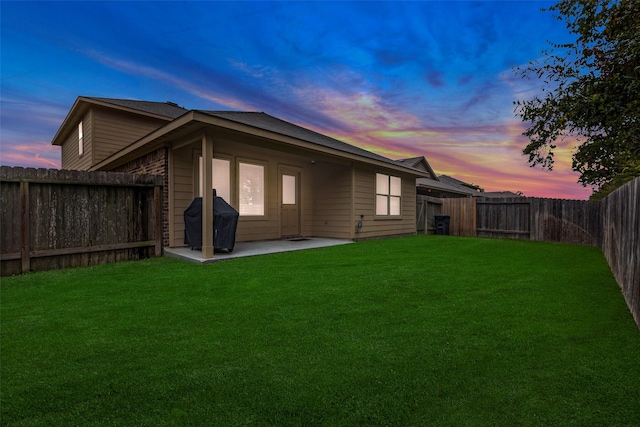 back house at dusk featuring a patio and a lawn