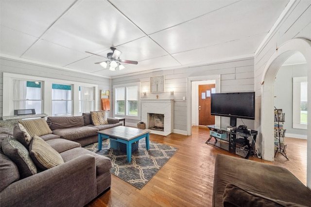 living room featuring hardwood / wood-style flooring, a brick fireplace, ceiling fan, and wood walls