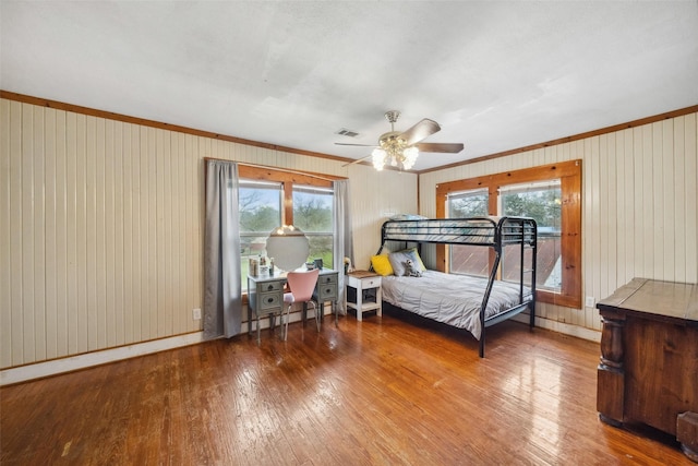 bedroom with ceiling fan, wood-type flooring, ornamental molding, and multiple windows