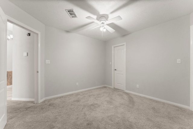 spare room with ceiling fan, a textured ceiling, light carpet, visible vents, and baseboards