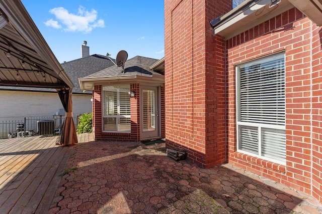 doorway to property with central air condition unit, brick siding, a patio, and roof with shingles