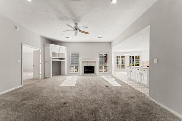 unfurnished living room featuring a textured ceiling, ceiling fan with notable chandelier, light carpet, and a tile fireplace