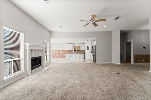 unfurnished living room featuring ceiling fan, a fireplace, light tile patterned floors, and plenty of natural light