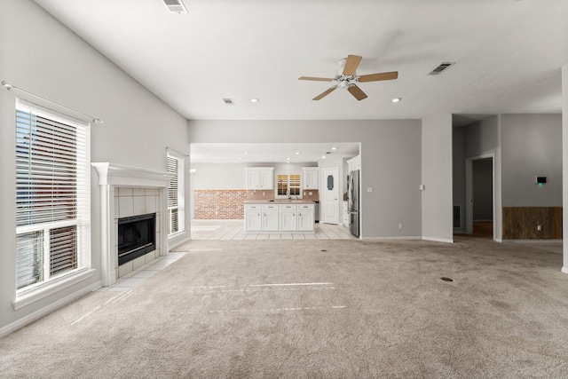 unfurnished living room featuring light carpet, a fireplace, visible vents, and ceiling fan