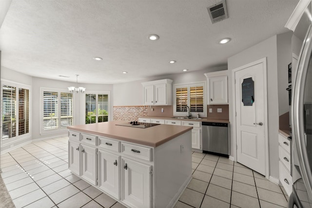 kitchen featuring visible vents, a center island, stainless steel appliances, white cabinetry, and a sink