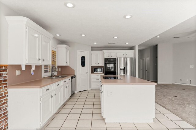 kitchen with light colored carpet, sink, black appliances, white cabinets, and a kitchen island