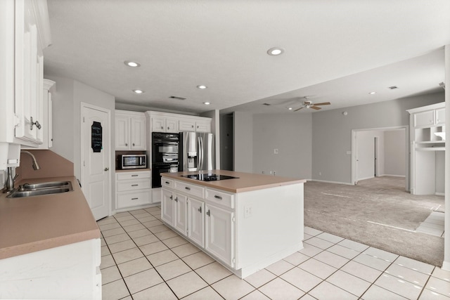 kitchen featuring light carpet, black appliances, sink, a kitchen island, and white cabinetry