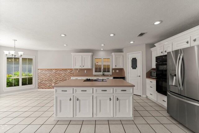 kitchen featuring brick wall, black appliances, an inviting chandelier, white cabinets, and a center island