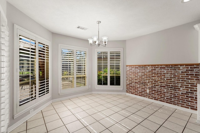 unfurnished dining area featuring light tile patterned floors, brick wall, and an inviting chandelier