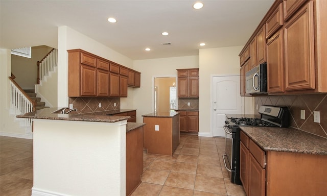 kitchen with a center island, dark stone countertops, light tile patterned floors, gas stove, and kitchen peninsula