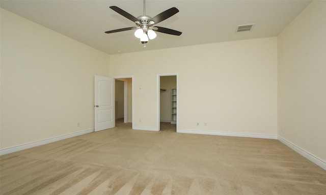 unfurnished bedroom featuring light carpet, a closet, a spacious closet, and ceiling fan