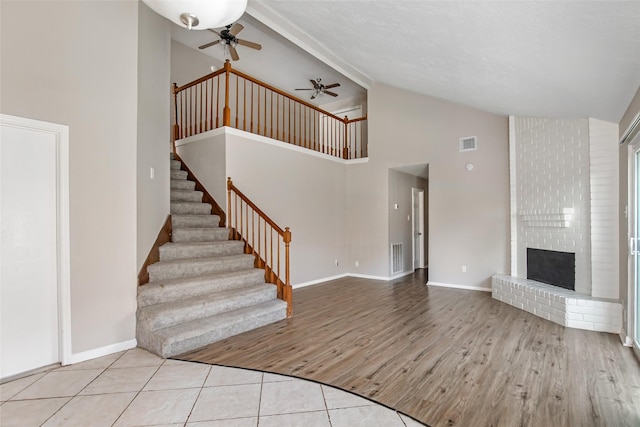 unfurnished living room with ceiling fan, light hardwood / wood-style floors, a towering ceiling, and a fireplace