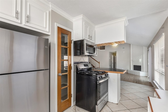 kitchen with lofted ceiling, light tile patterned floors, white cabinetry, stainless steel appliances, and a fireplace