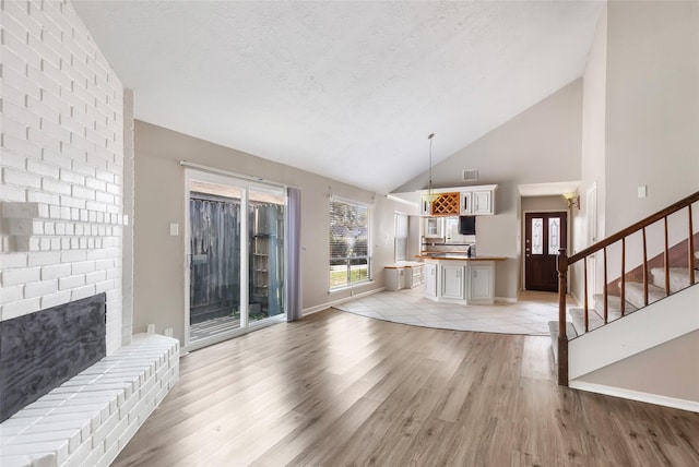 unfurnished living room with a healthy amount of sunlight, high vaulted ceiling, a textured ceiling, and light wood-type flooring