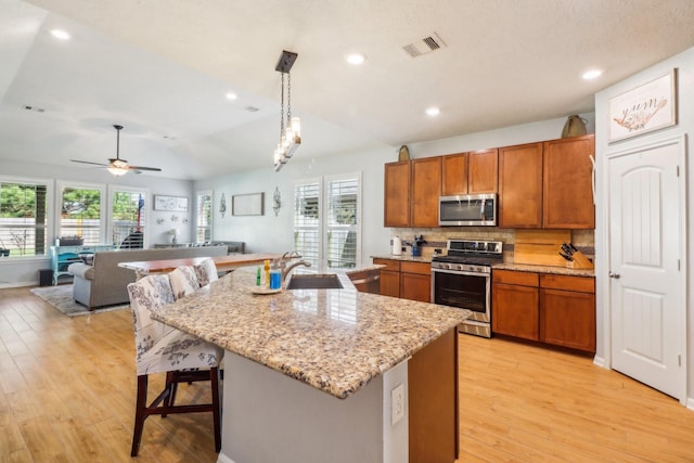 kitchen featuring ceiling fan, sink, hanging light fixtures, stainless steel appliances, and a kitchen island with sink