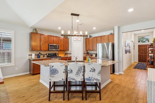 kitchen with a center island with sink, sink, decorative backsplash, decorative light fixtures, and stainless steel appliances