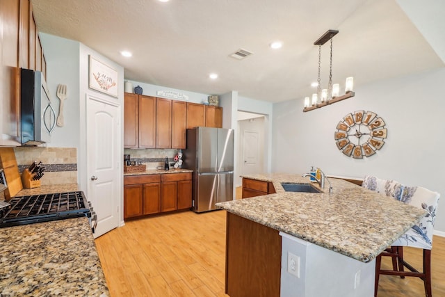 kitchen featuring sink, hanging light fixtures, backsplash, a kitchen island with sink, and appliances with stainless steel finishes