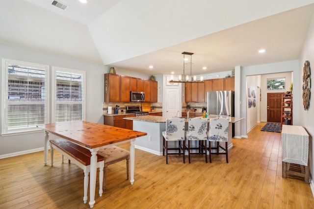 kitchen with backsplash, a kitchen island with sink, hanging light fixtures, vaulted ceiling, and stainless steel appliances